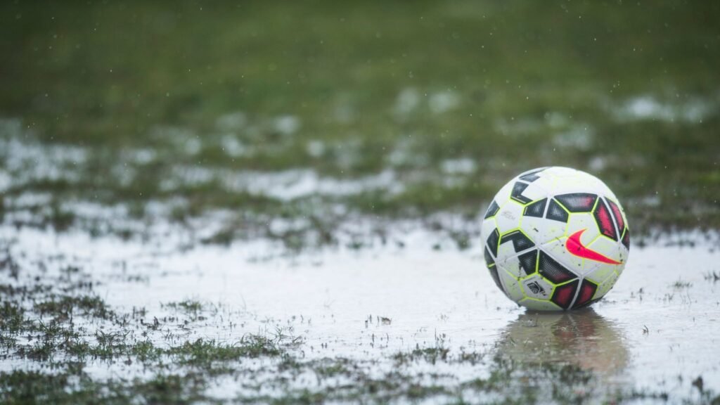 A football sitting in a large muddy puddle in the rain
