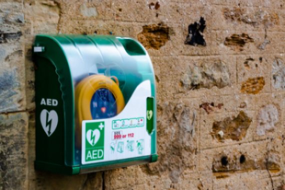 A green AED box on an old brick wall.